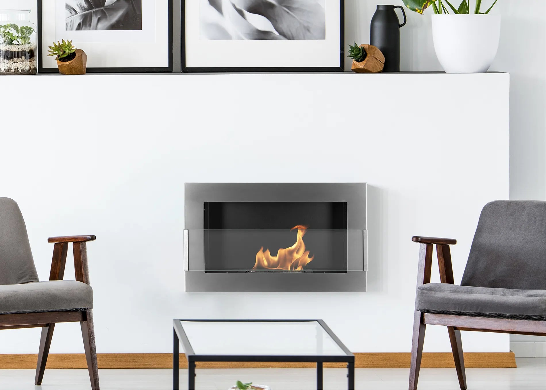 Modern living room with a wall-mounted inox biofireplace, gray chairs, and a glass coffee table.