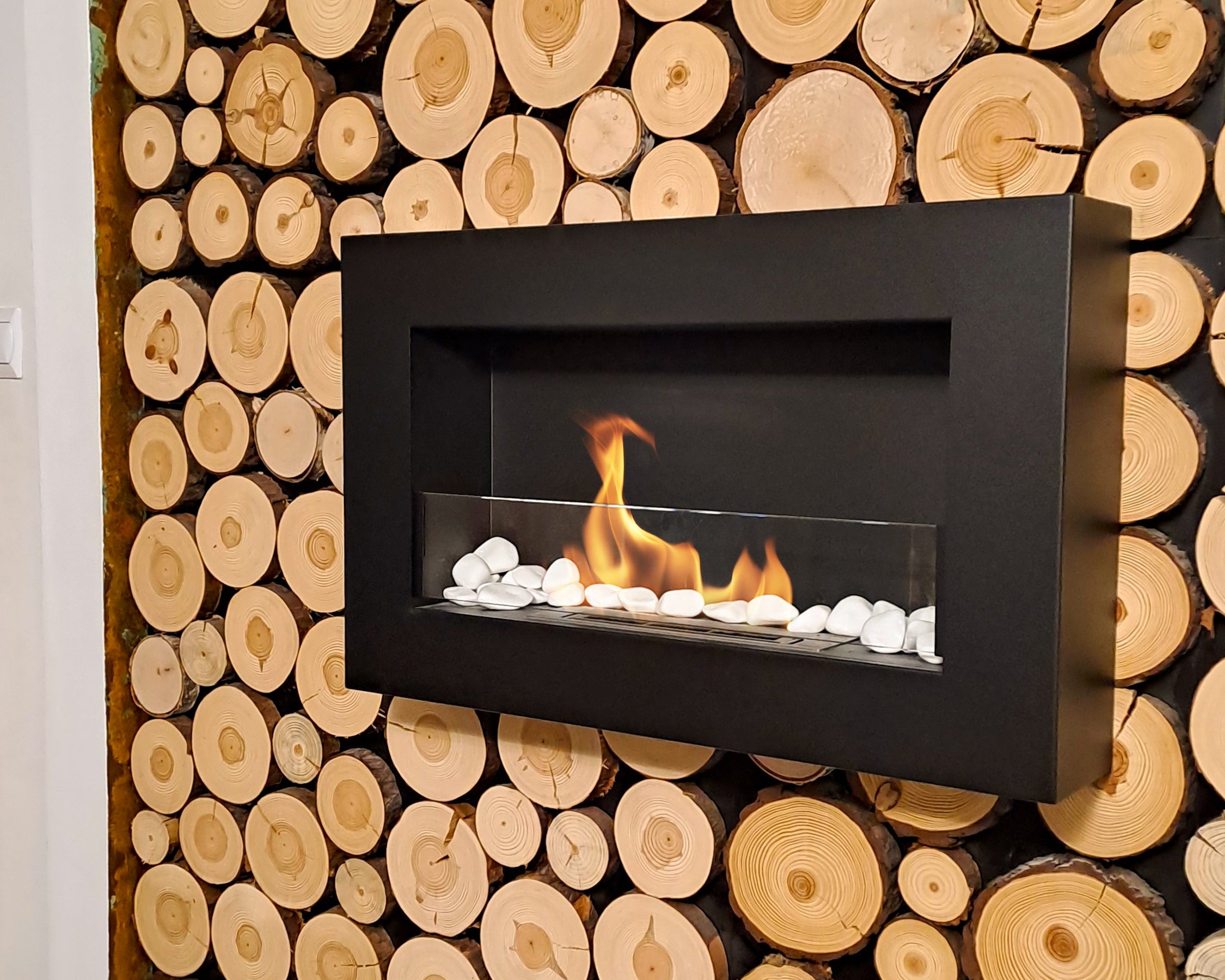 Modern black biofireplace embedded in a wall made of stacked wooden logs