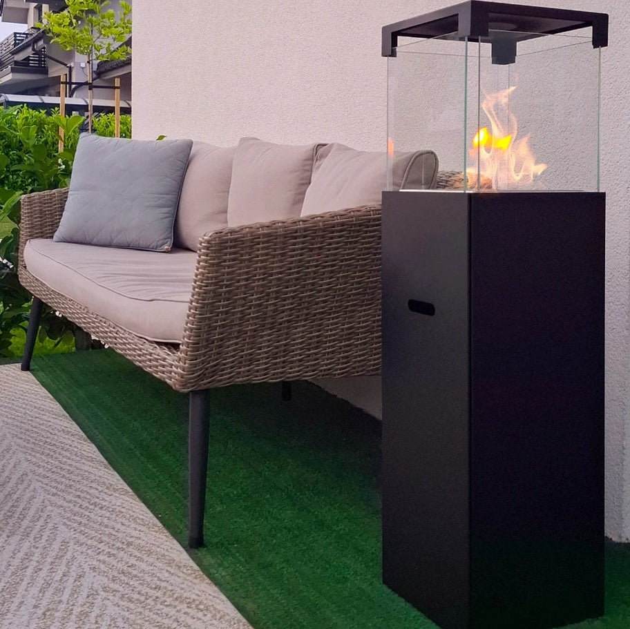 Outdoor patio with wicker sofa, small table, and fire pit on a green lawn.