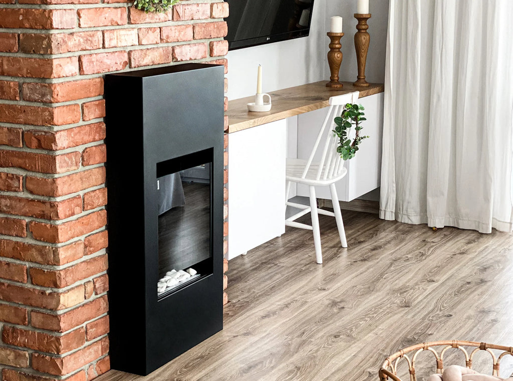 Angled view of the unlit MODERN black bioethanol fireplace beside a brick wall, with white decorative stones inside
