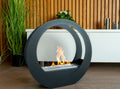 ONLY matt black circular bioethanol fireplace with a lit flame in front of a white cabinet and wooden slat wall
